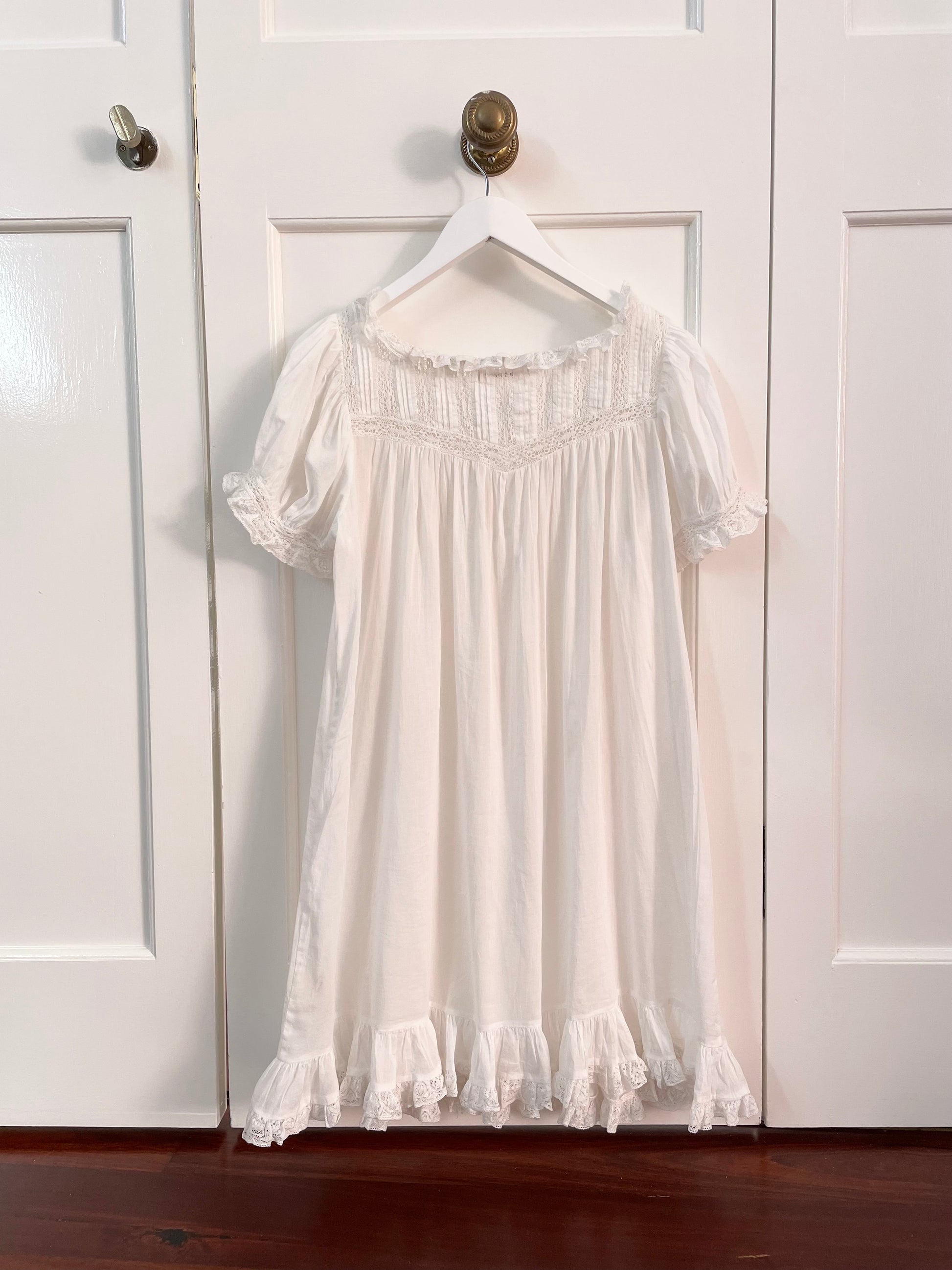 Back view of white cotton DÔEN dress with short puffed sleeves trimmed with lace and ruffles